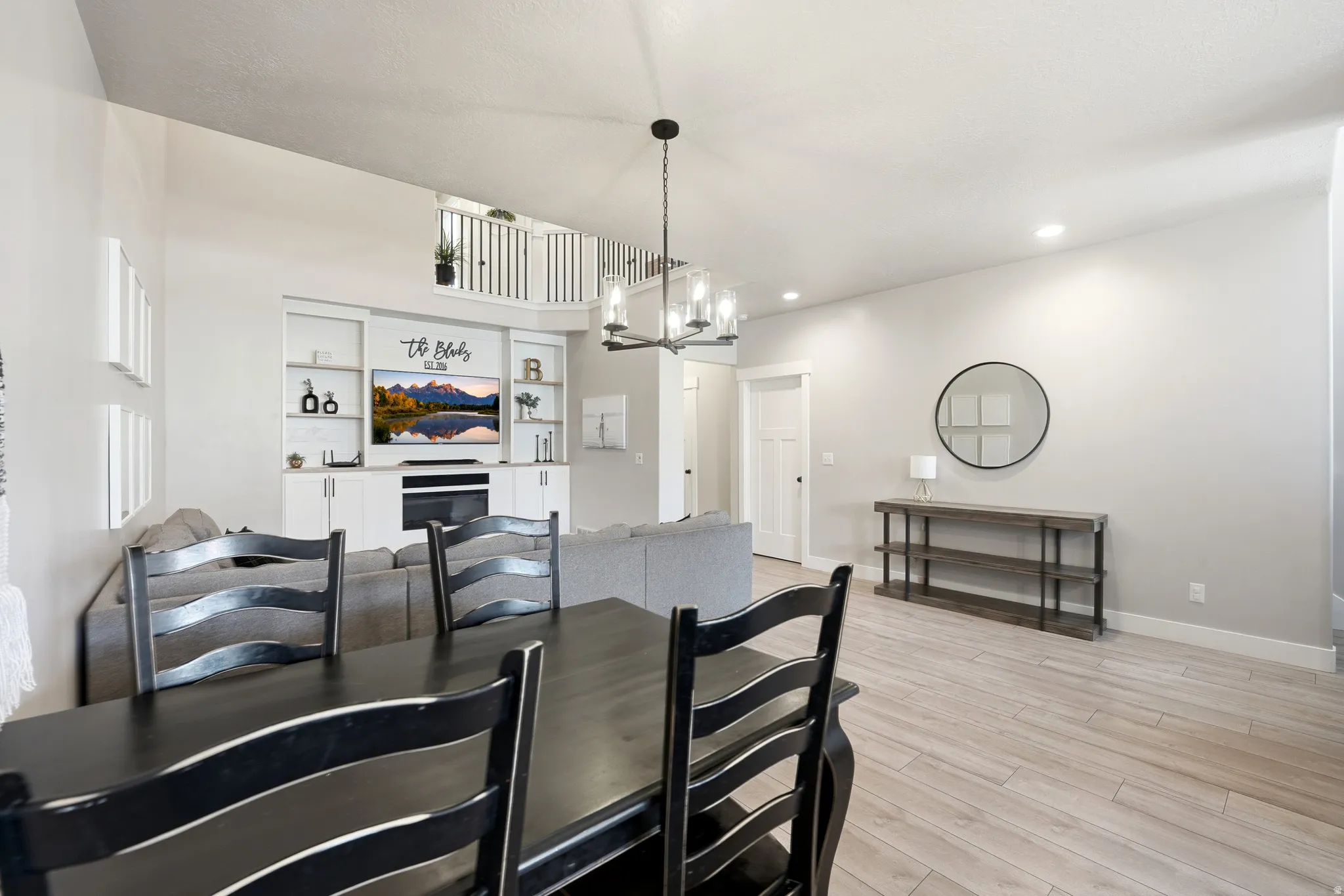 Open-concept living area featuring light wood-finish flooring, a contemporary chandelier, recessed lighting, and a built-in media center with shelving and storage cabinetry