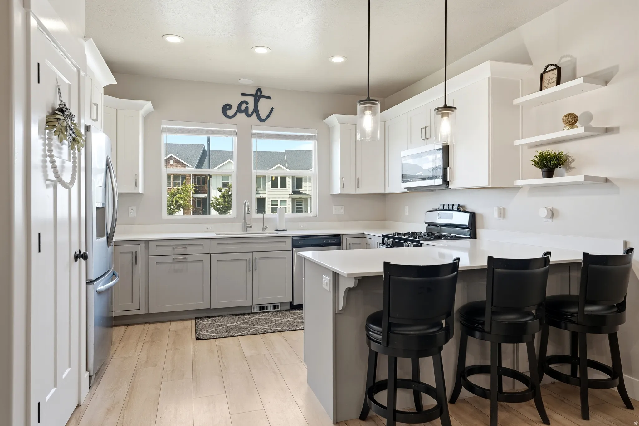 Contemporary kitchen featuring light wood-finish flooring, two-tone cabinetry with white upper and gray lower cabinets, and a kitchen island with seating