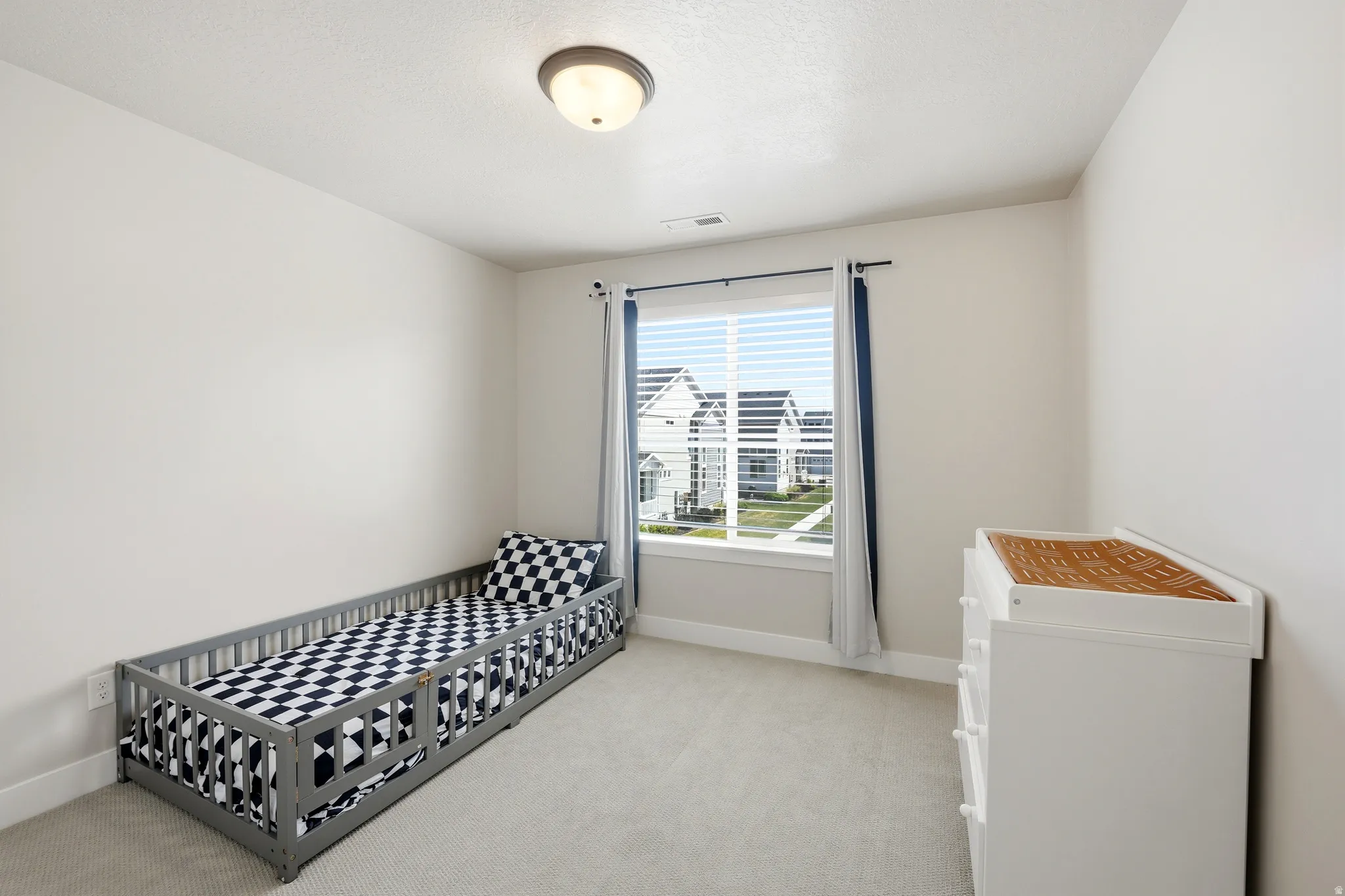 Neutral-toned room featuring a single window with blinds, light gray carpeting, and a flush mount ceiling light