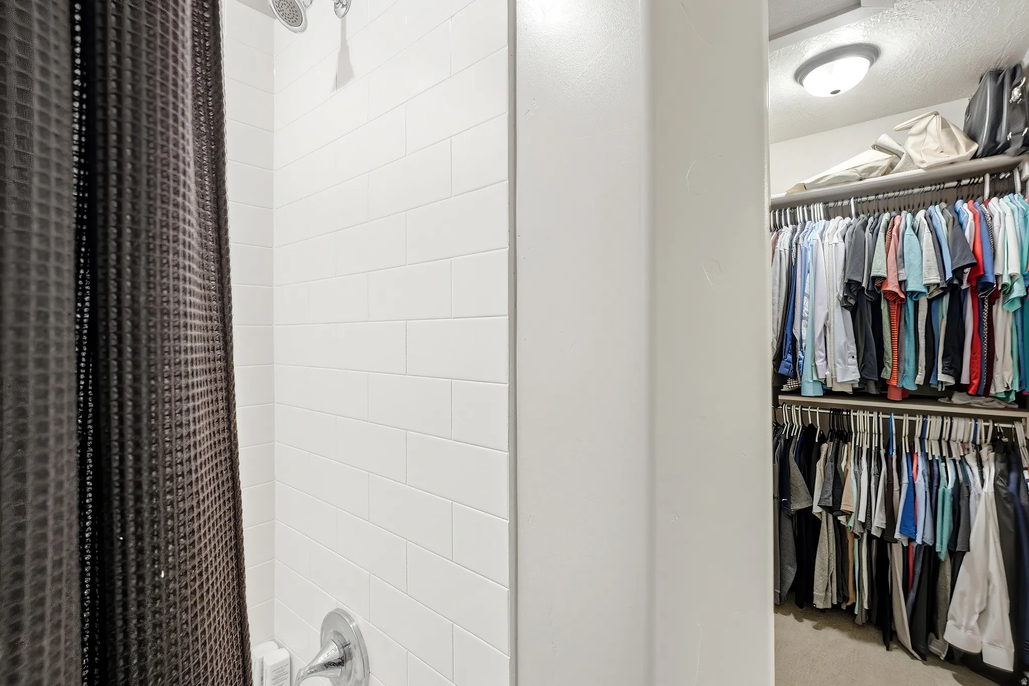 White subway tile shower enclosure with chrome fixtures and an adjacent walk-in closet featuring built-in shelving and hanging rods