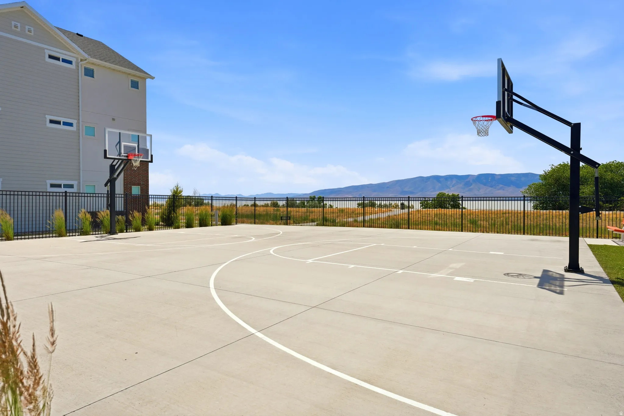 Full-size concrete basketball court with dual hoops, black perimeter fencing, and distant mountain scenery