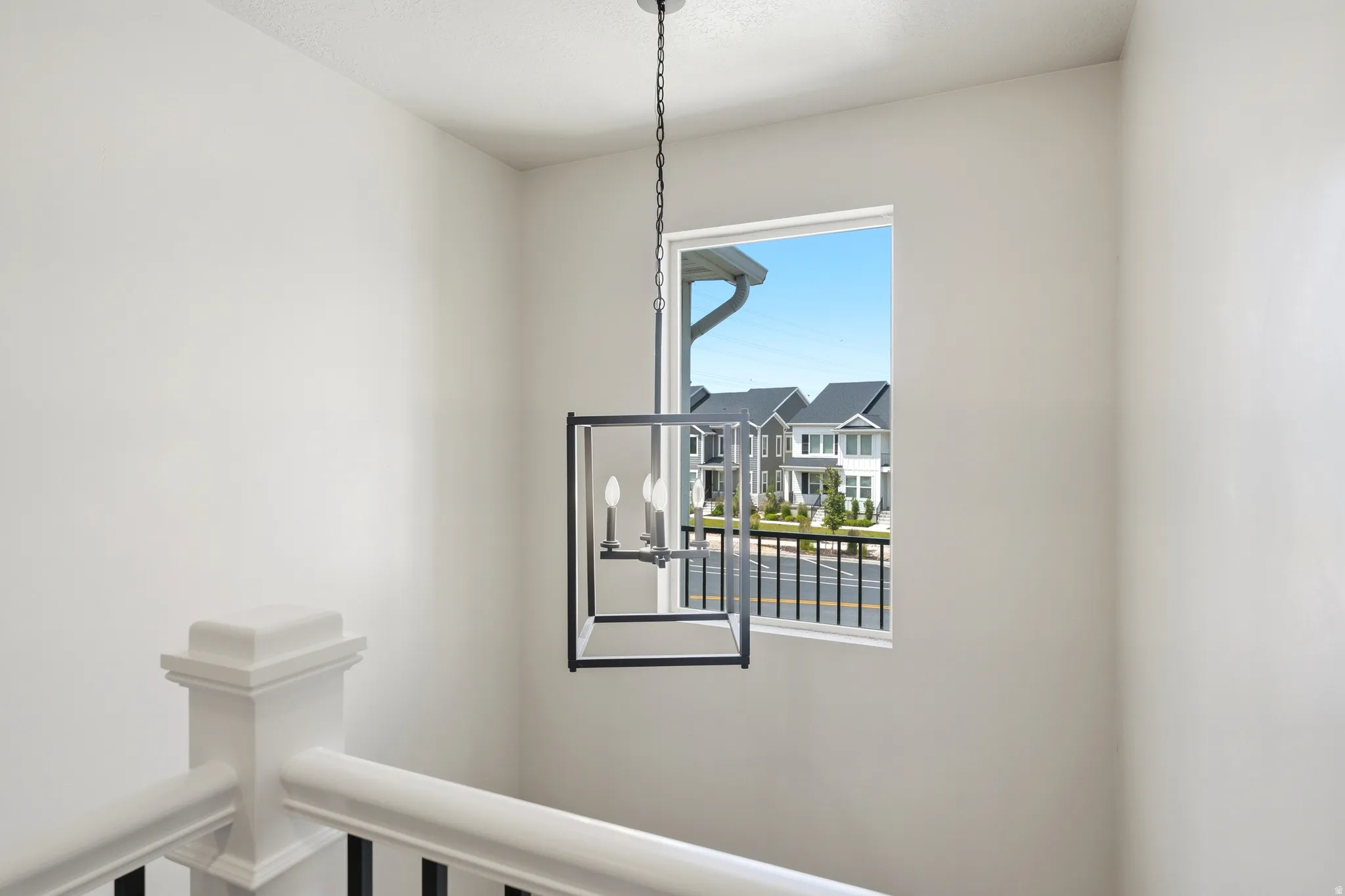 Stairwell featuring a contemporary black lantern chandelier, white balustrade with black spindles, and a window overlooking a street with residential homes