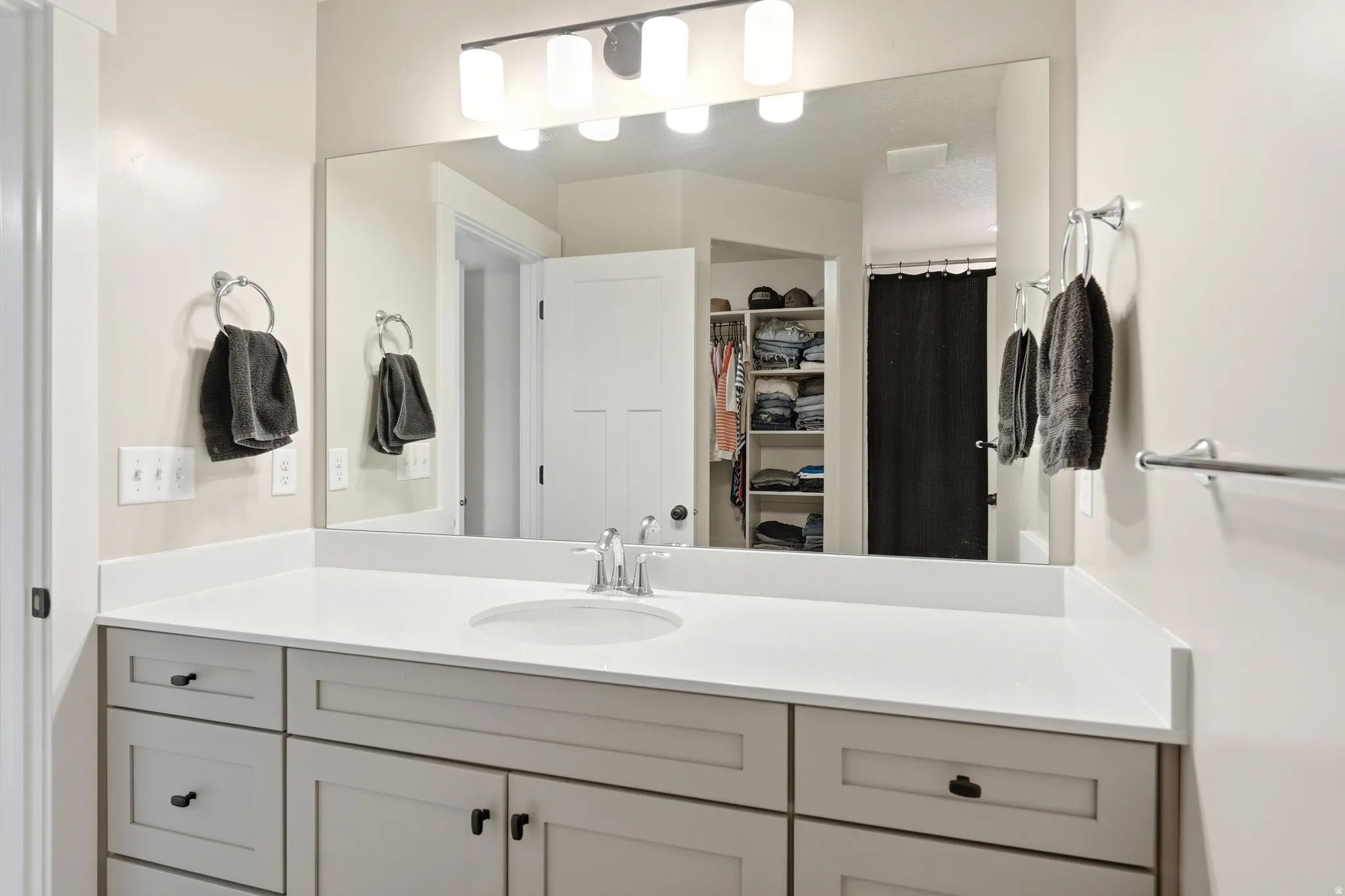 Bathroom vanity featuring a single basin, light-toned countertop, and light gray cabinetry with dark hardware