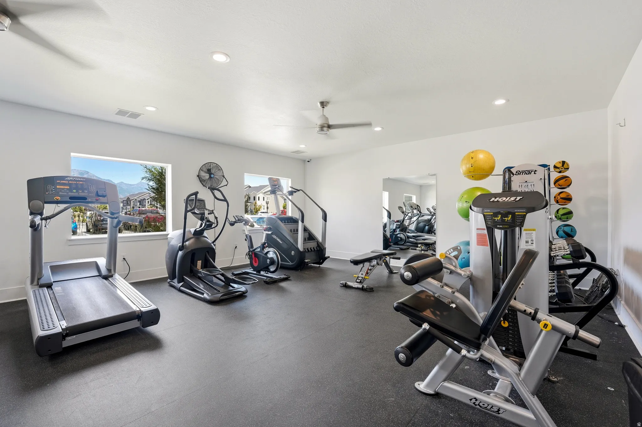 Spacious fitness room featuring rubber flooring, multiple windows, recessed lighting, and ceiling fans