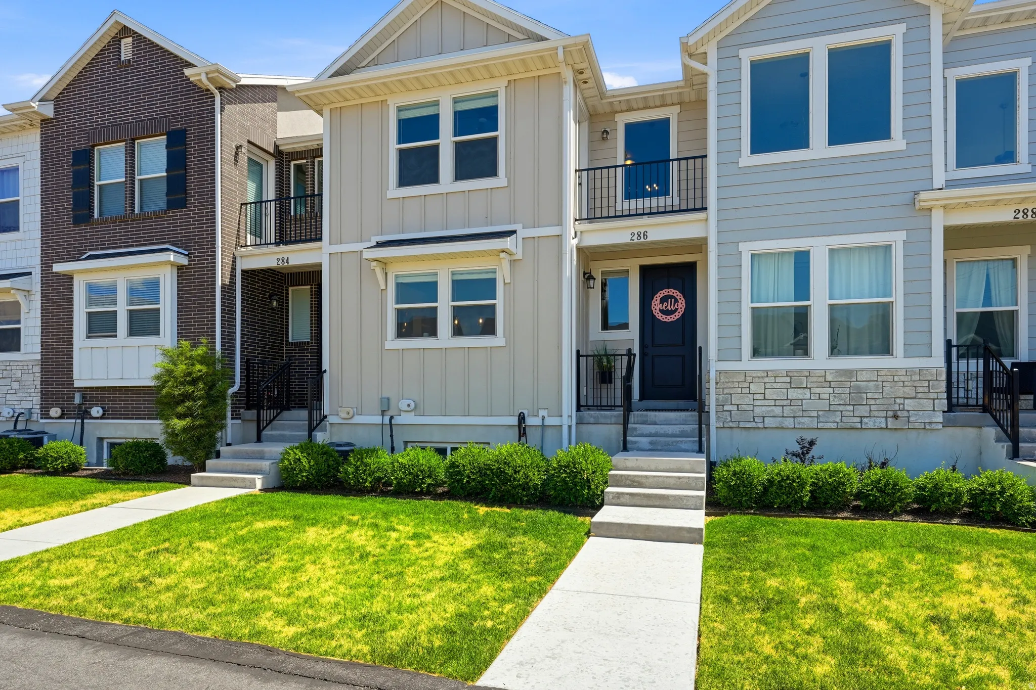 Contemporary townhome facade featuring light-colored siding, contrasting black front door, and a second-story balcony with black railings
