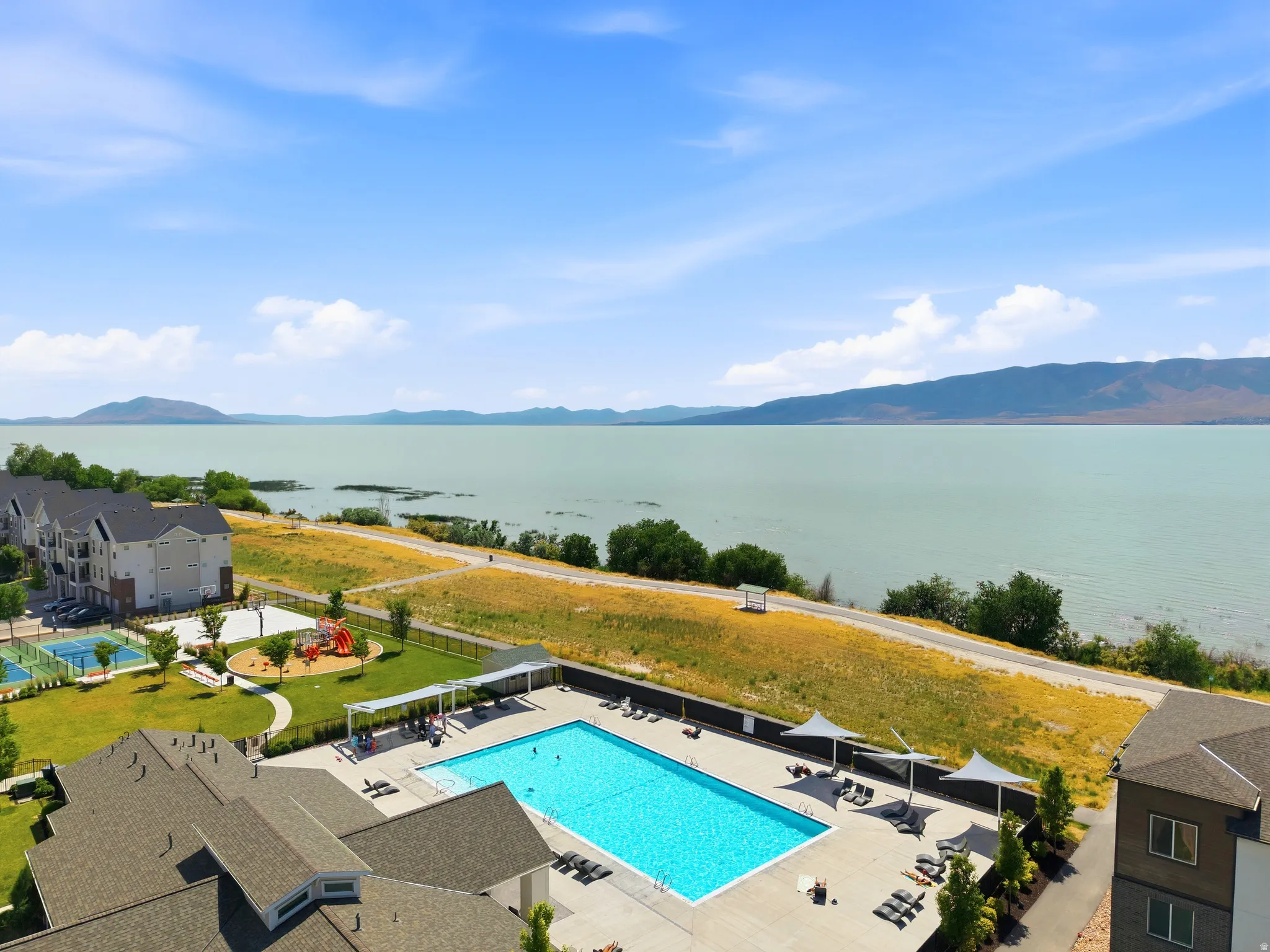 Outdoor swimming pool with lounge seating and shade structures, bordered by a large body of water