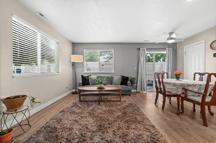 Open-concept living space featuring wood-finish flooring, multiple windows with blinds, a ceiling fan with integrated lighting, and a sliding glass door