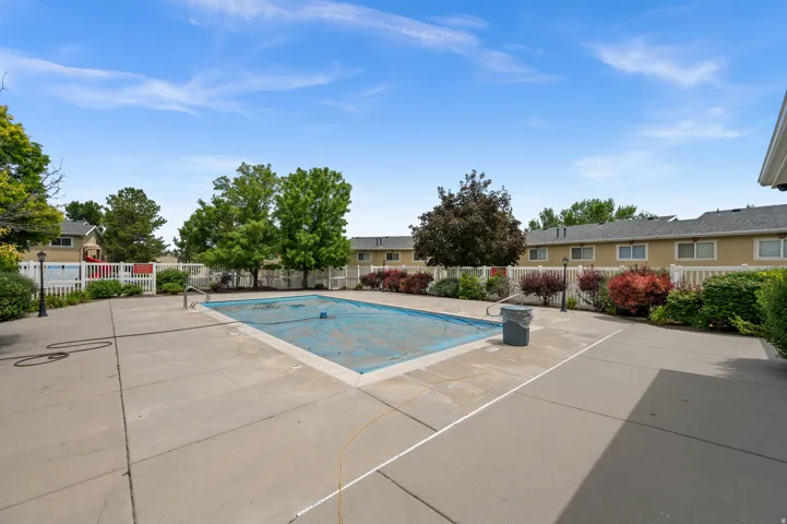 Outdoor pool area featuring a concrete surround, white picket fencing, and mature landscaping