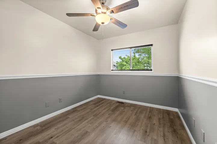 Room featuring wood-finish flooring, two-tone wall paint with white trim, and a window with blinds