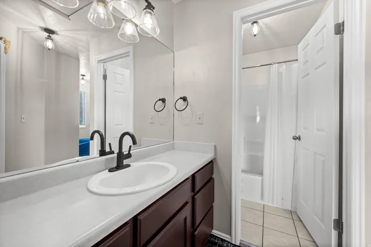Bathroom vanity featuring an integrated sink, dark wood-finish cabinetry, a full-width wall mirror, and matte black fixtures