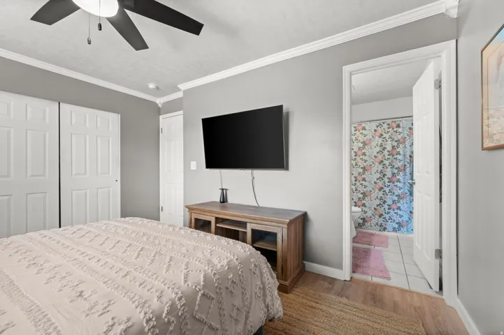 Bedroom featuring wood-finish flooring, a ceiling fan with integrated lighting, bi-fold closet doors, and crown molding