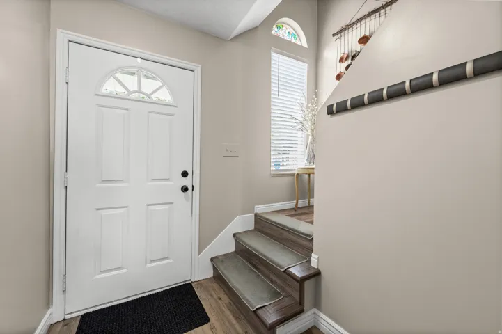 Entryway featuring a white paneled door with an arched glass insert, wood-finish flooring, and a staircase with individual carpet treads