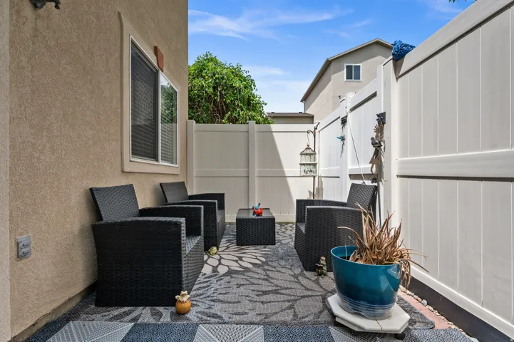 Private outdoor patio area featuring textured stucco exterior, a large window with blinds, and white vinyl perimeter fencing