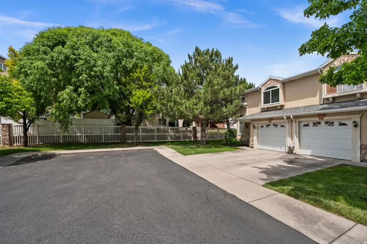 Stucco exterior featuring dual two-car garages with paneled doors, arched window accents, and mature trees