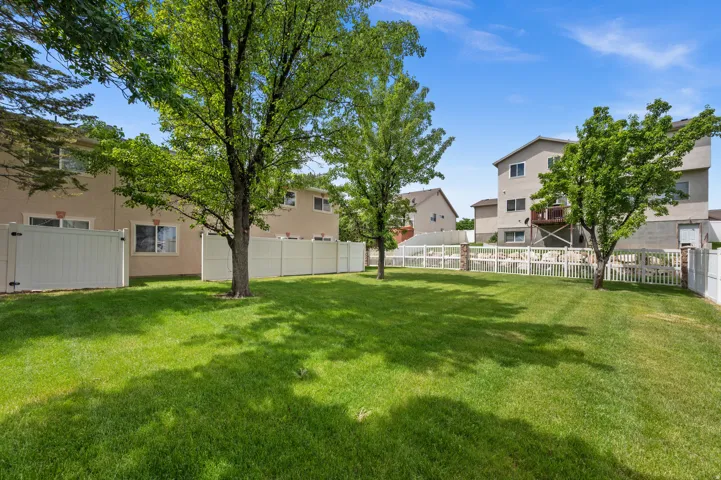 Expansive grassy yard featuring mature trees and white privacy fencing