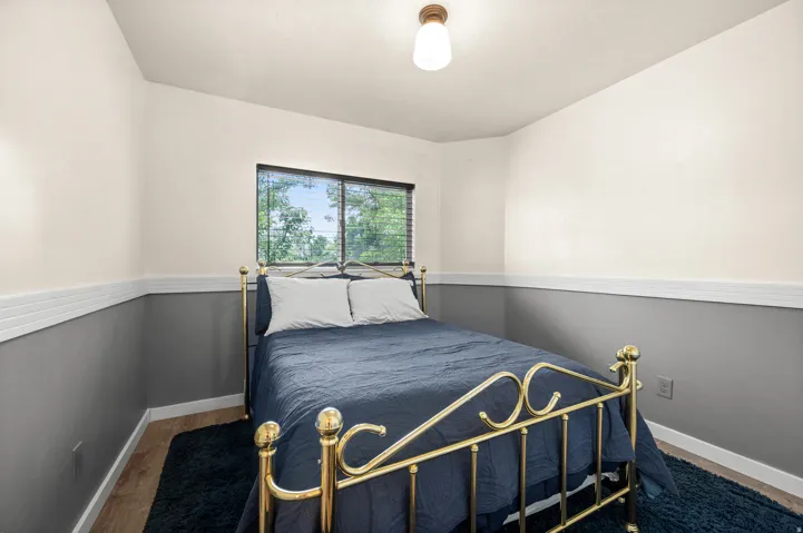 Bedroom featuring a two-tone wall design with wainscoting, wood-finish flooring, and a single window with blinds