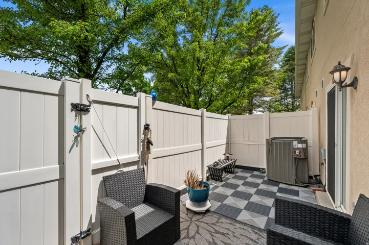 Private patio area featuring checkerboard-patterned flooring, perimeter fencing, and exterior wall lighting