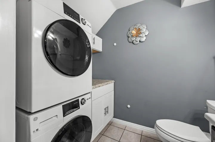 Laundry area featuring stacked front-load washer and dryer units, white cabinetry, and a light-colored countertop