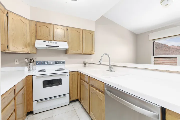 Kitchen featuring light wood cabinetry, white countertops, a white electric range, and a stainless steel dishwasher