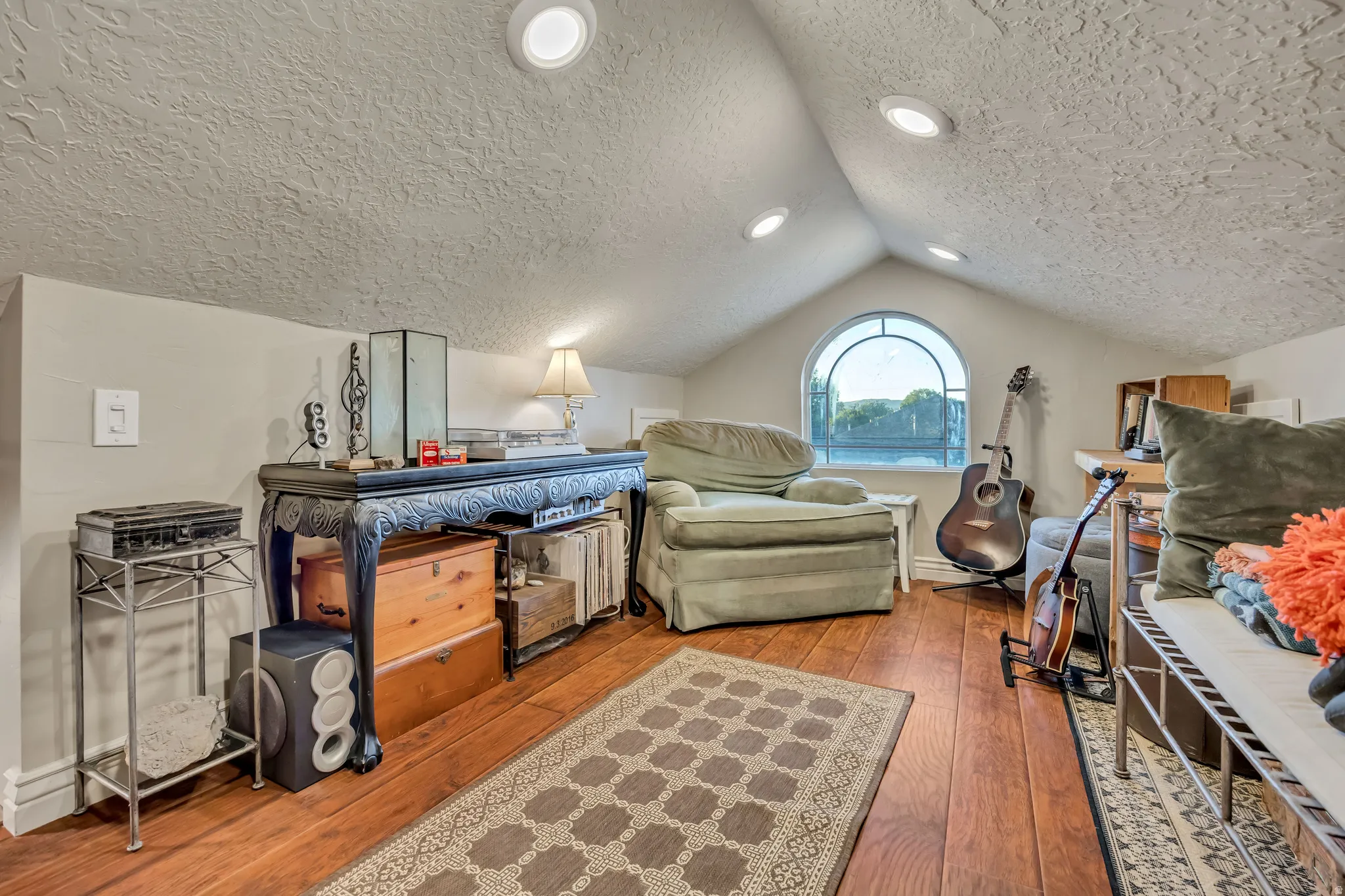 Attic space featuring wood-finish flooring, recessed lighting, and a prominent arched window