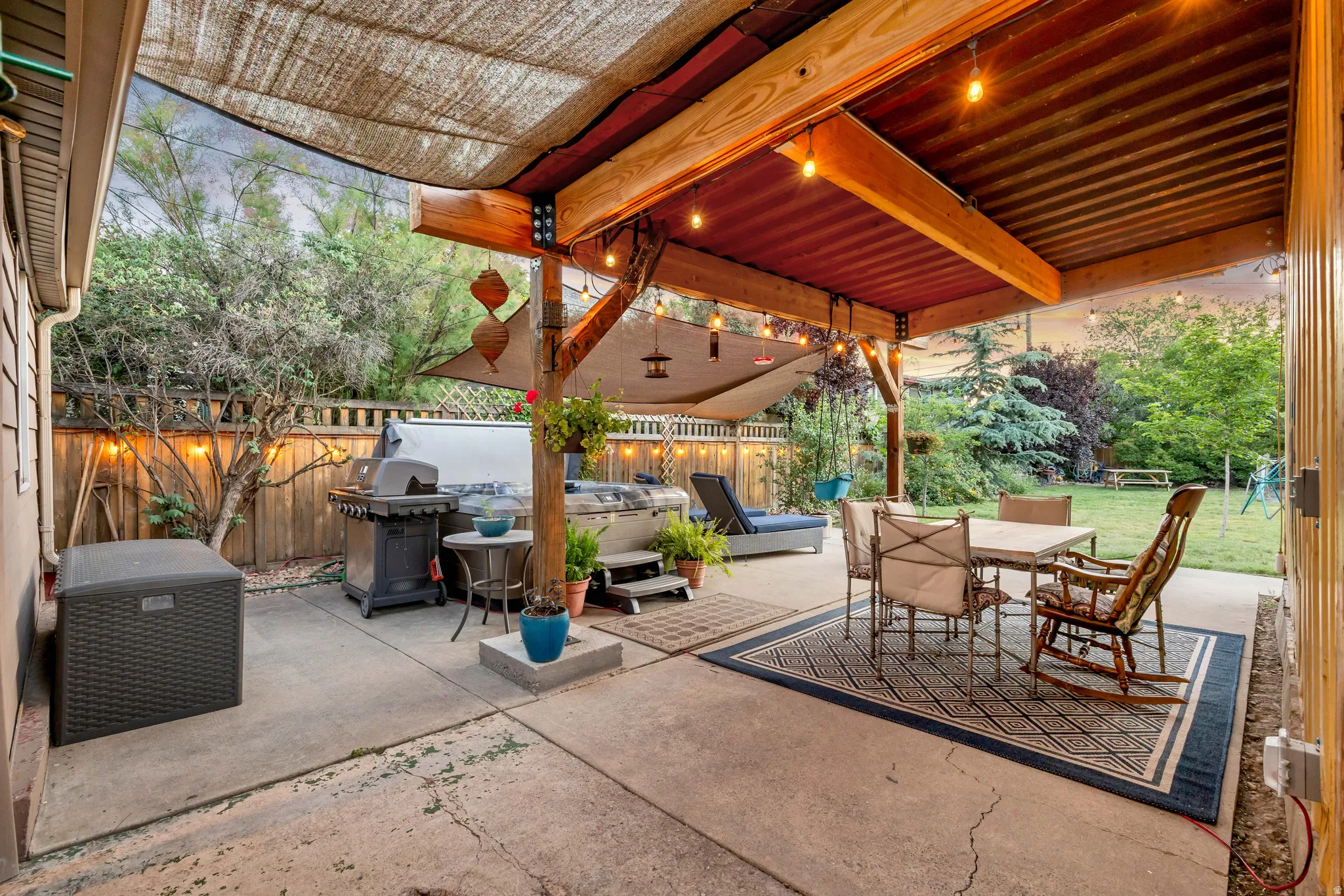 Expansive concrete patio featuring a wood-beamed covered area with string lights and a shade sail