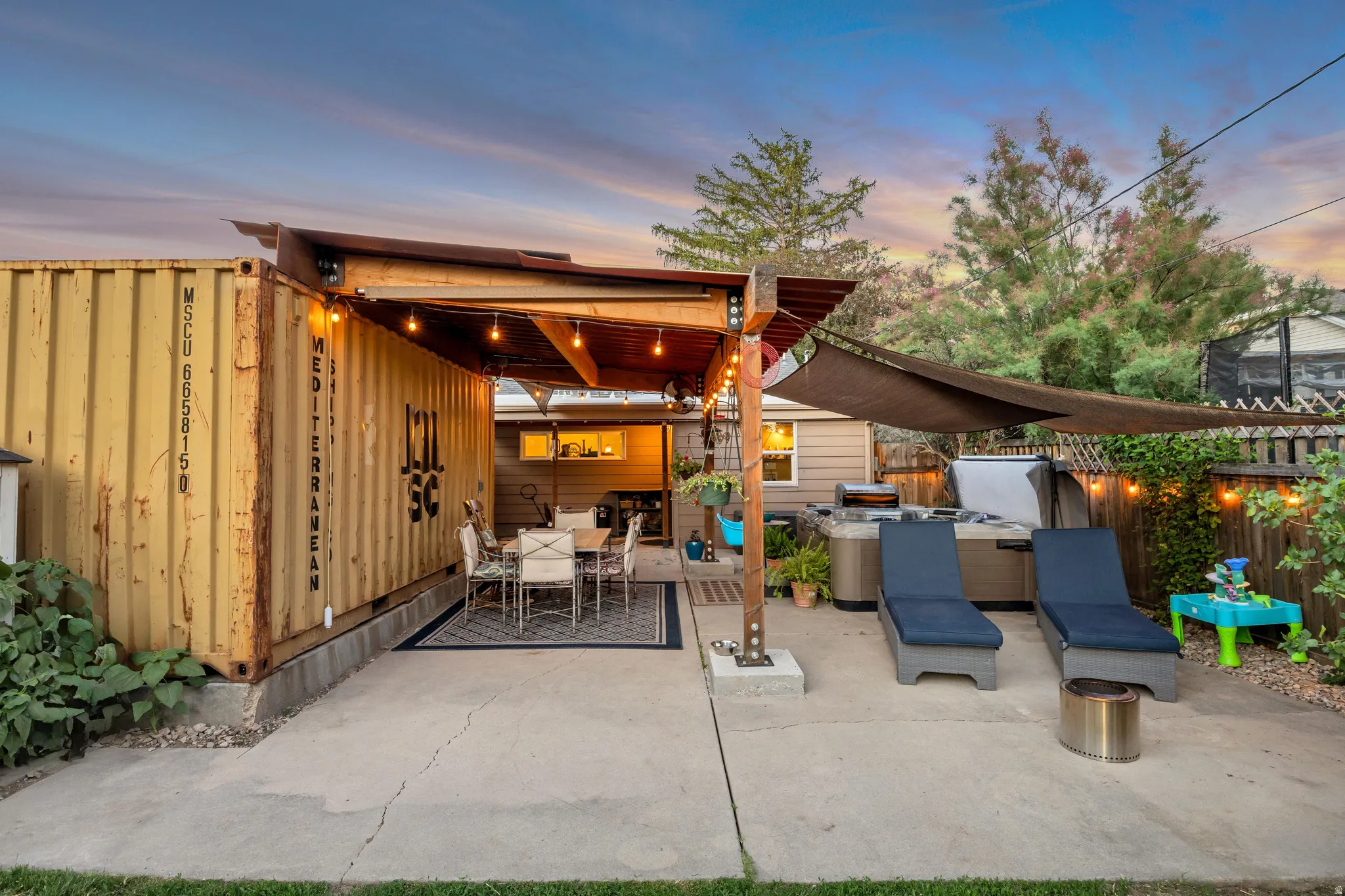 Expansive concrete patio area featuring a covered dining space integrated with a shipping container structure