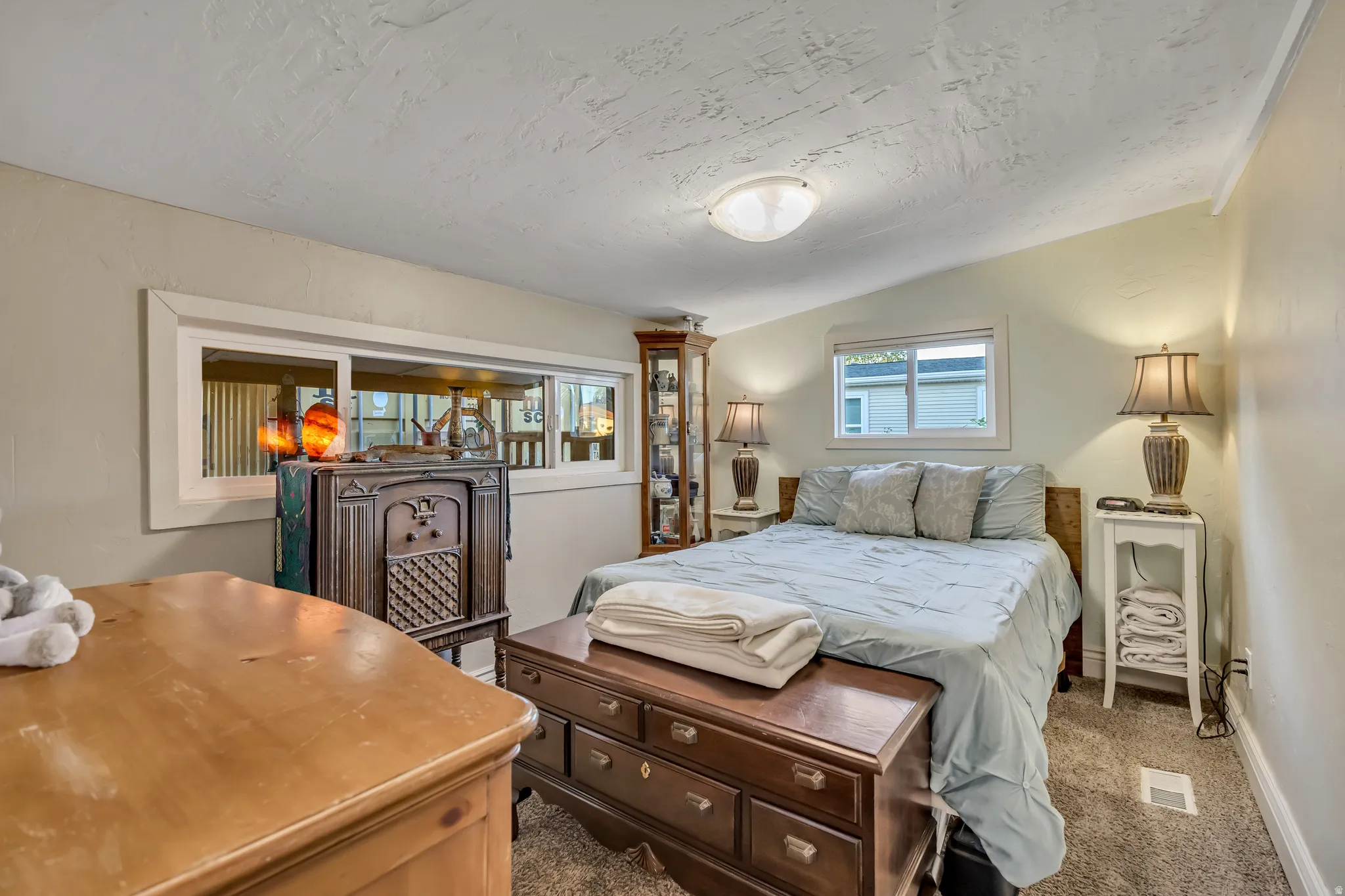 Carpeted bedroom featuring a textured ceiling, a built-in recessed window, and two permanent windows with white trim