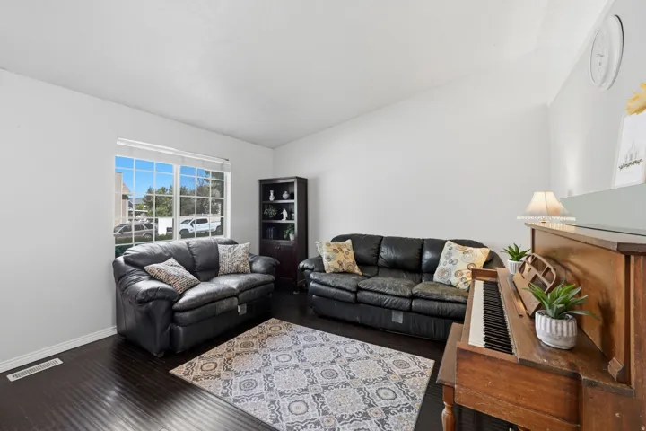 Spacious living area featuring dark wood-finish flooring, white wall tones, and a large multi-pane window