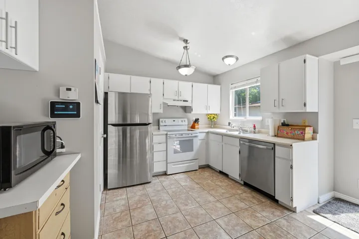 Kitchen featuring white cabinetry, stainless steel refrigerator and dishwasher, white range, and tiled flooring