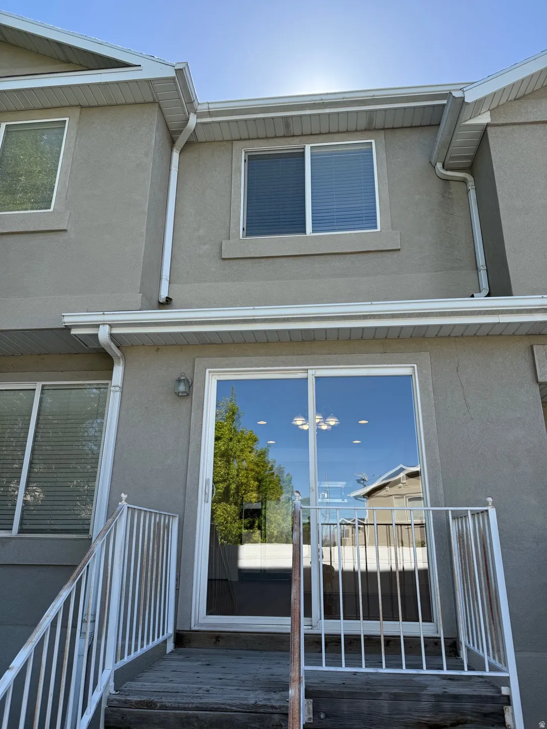Rear stucco exterior featuring a sliding glass door, white window frames, and exterior lighting
