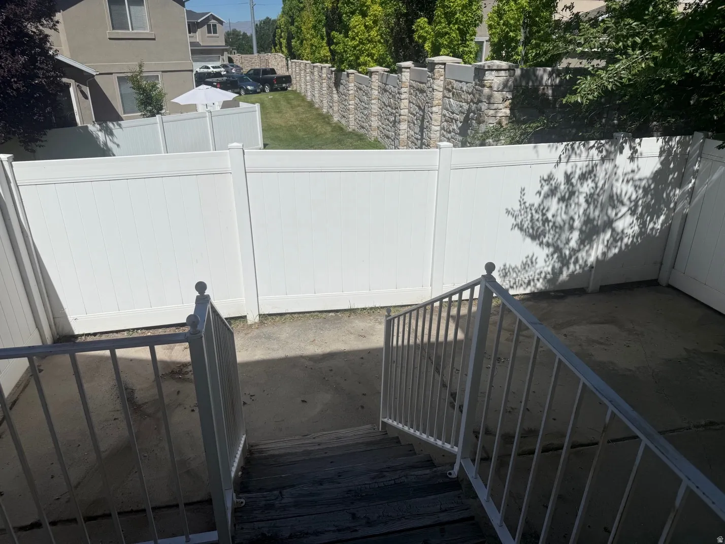 Rear concrete patio area featuring white vinyl fencing and a stone retaining wall