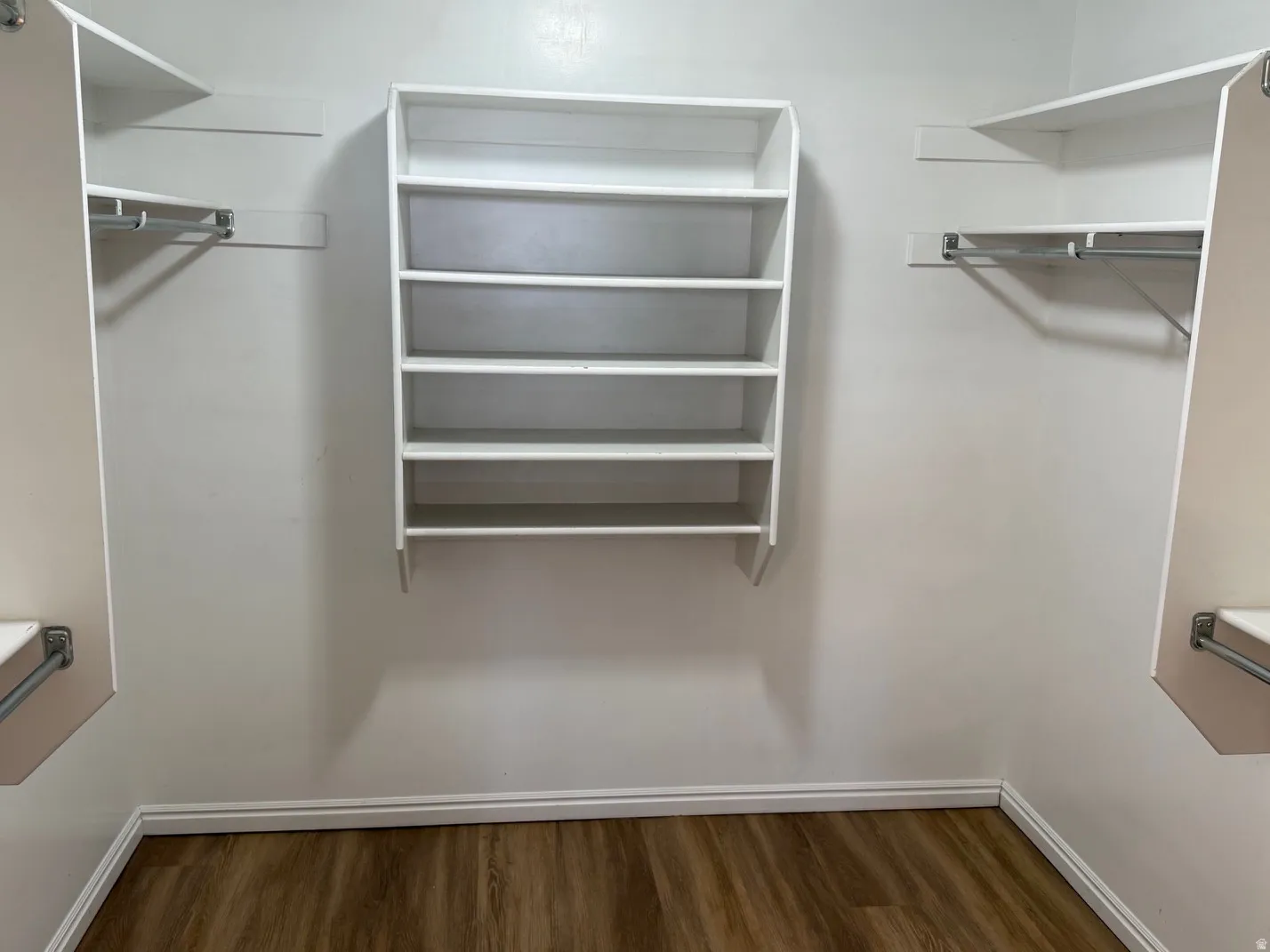 Walk-in closet featuring wood-finish flooring, white baseboards, and a center shelving unit