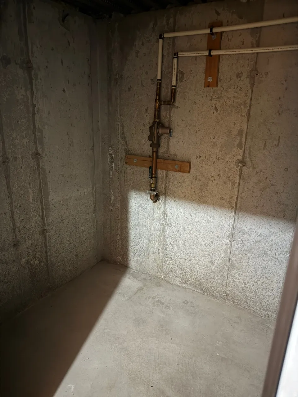 Concrete-walled utility space with exposed copper and PVC piping