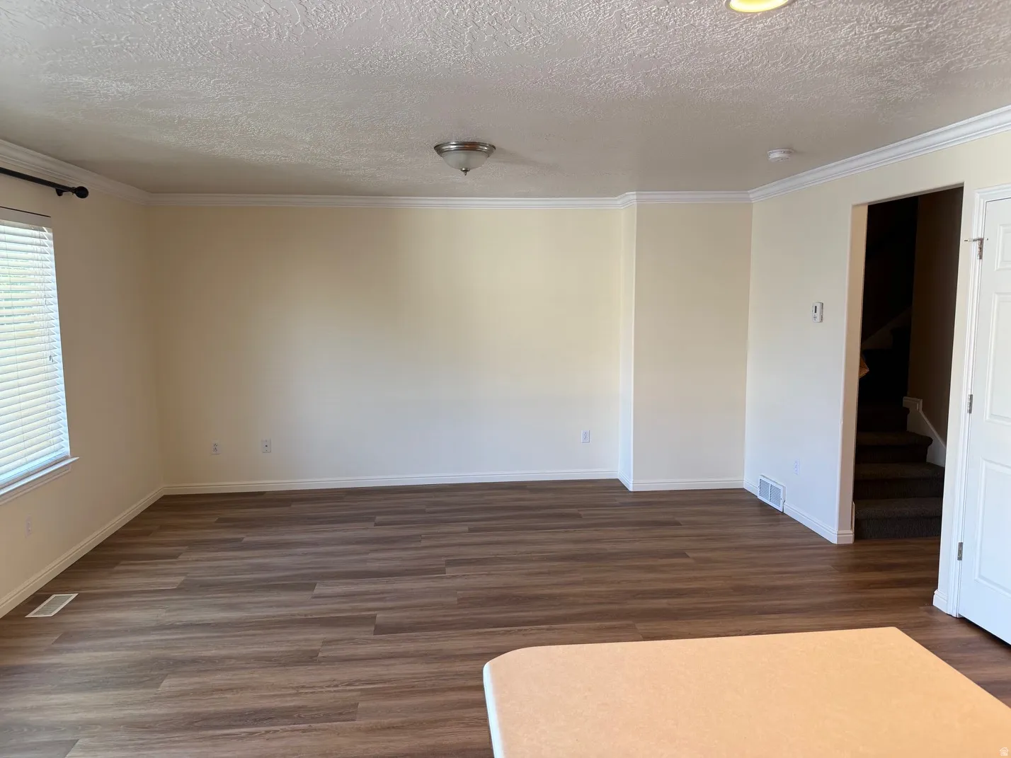 Spacious interior room featuring wood-finish flooring, white baseboards, and crown molding