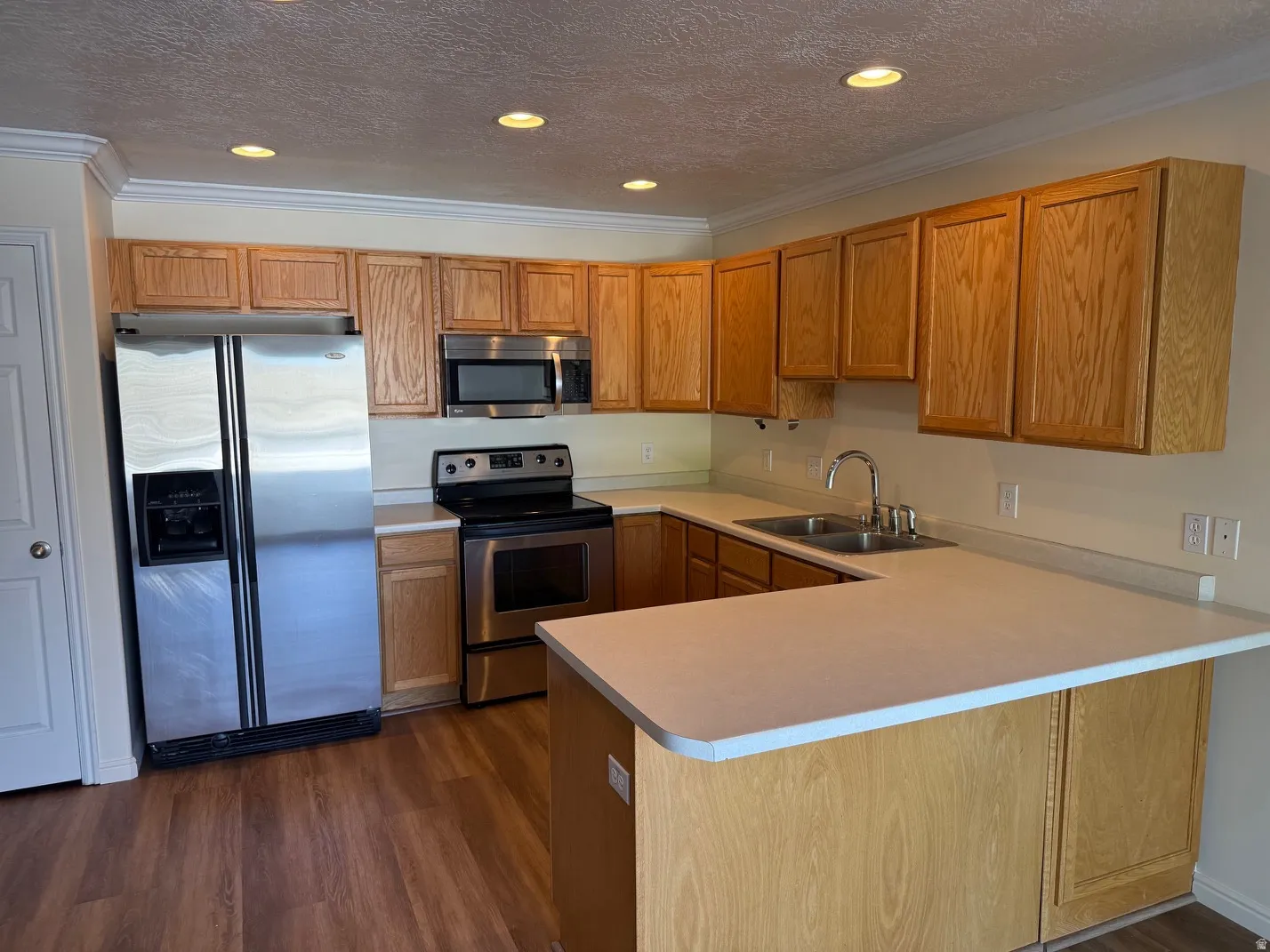 Kitchen featuring wood-finish flooring, stainless steel appliances, light wood cabinetry, and a double basin sink