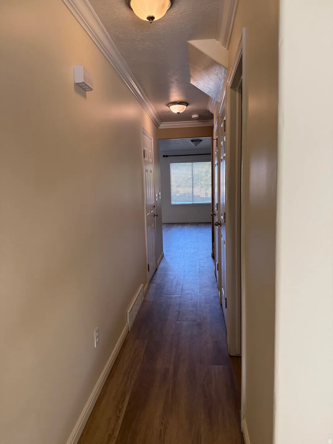 Hallway featuring wood-finish flooring, neutral wall paint, white baseboards, and crown molding