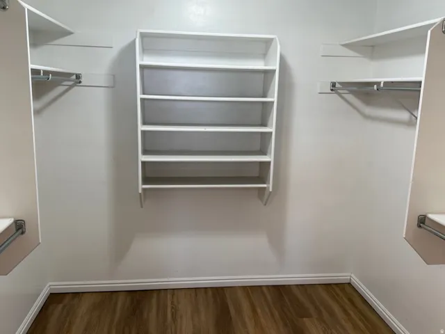 Walk-in closet featuring wood-finish flooring, white baseboards, and a center shelving unit