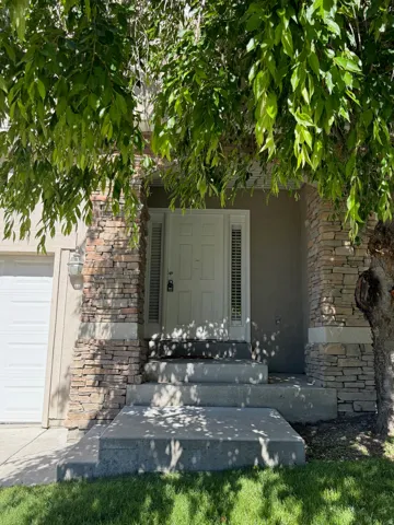 Front entry featuring a paneled door with sidelights, stacked stone accents on architectural columns, a stepped concrete walkway, and a garage with a white sectional door