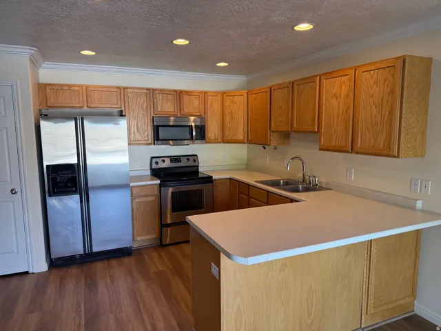 Kitchen featuring wood-finish flooring, stainless steel appliances, light wood cabinetry, and a double basin sink