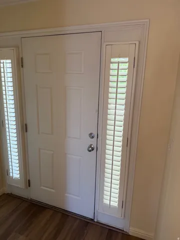 Entryway featuring a paneled door, two sidelight windows with plantation shutters, wood-finish flooring, and crown molding