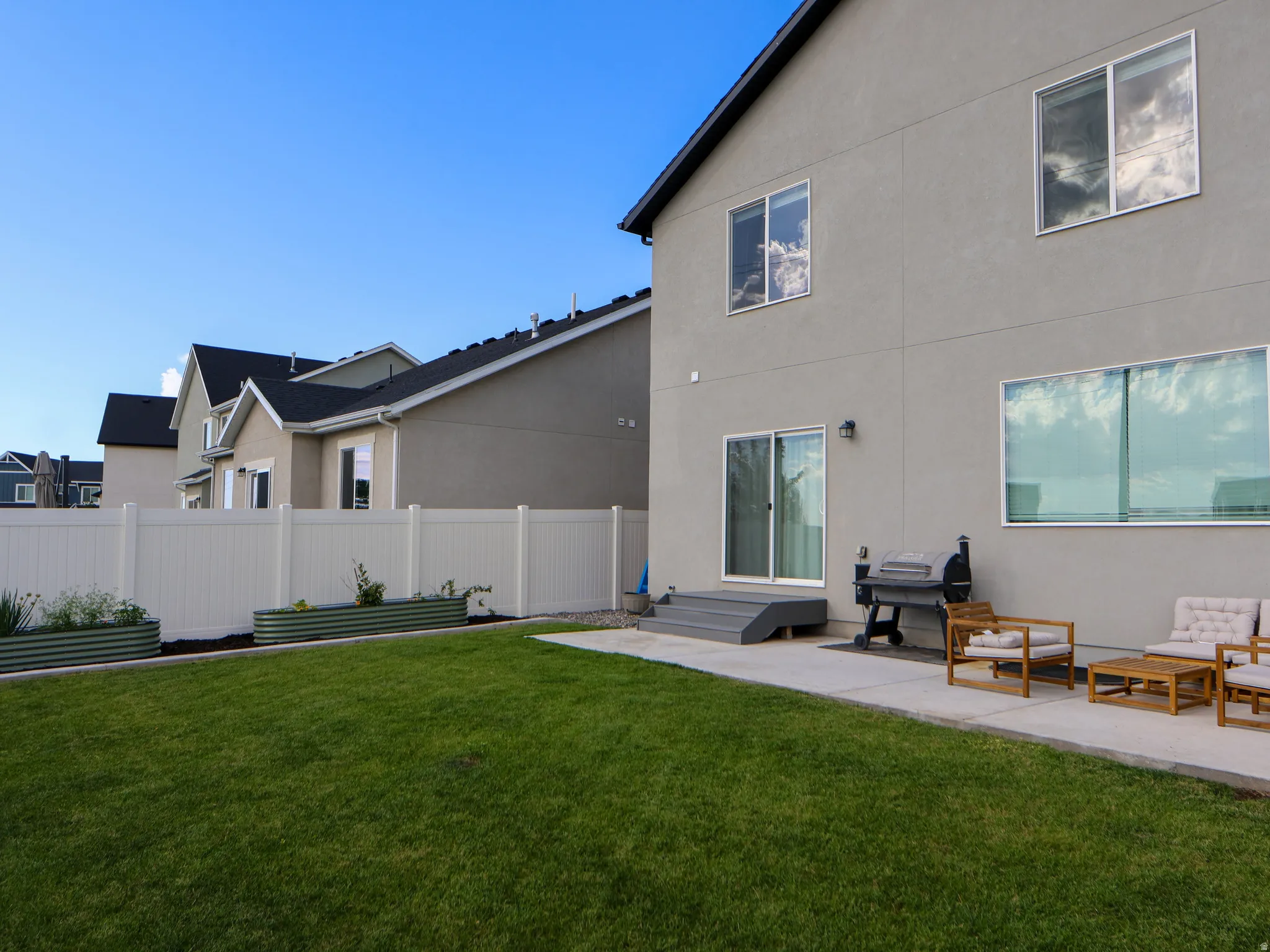 Backyard with patio, white vinyl fencing, and two raised garden beds