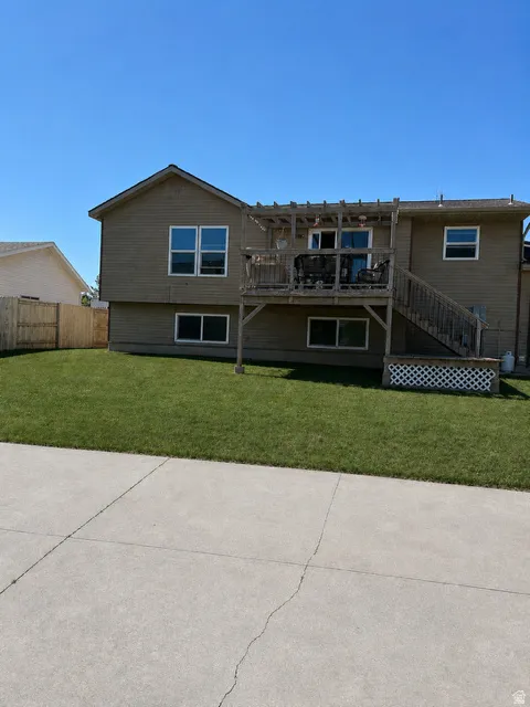 Rear exterior featuring a multi-level wood deck with pergola, tan siding, and a manicured lawn