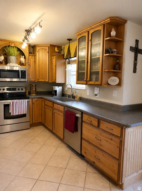 Kitchen featuring wood cabinetry, stainless steel appliances, dark countertops, and ceramic tile flooring