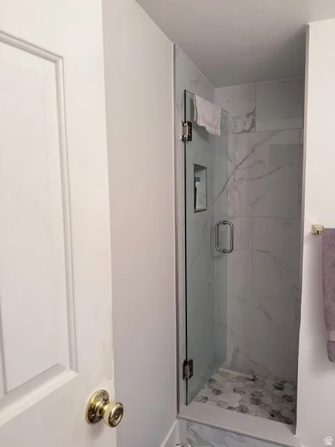 Glass-enclosed shower with a built-in niche, featuring marble-style wall tiles and hexagonal floor tiles