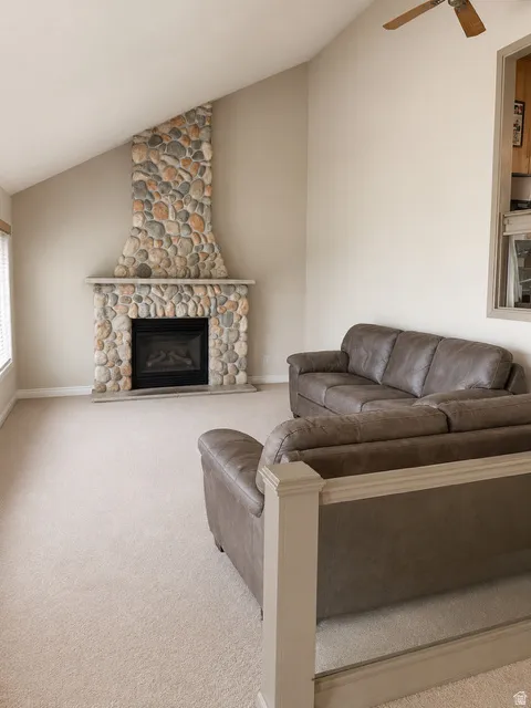 Living area featuring an angled stone fireplace with a black firebox, vaulted ceiling, and neutral-toned carpeting