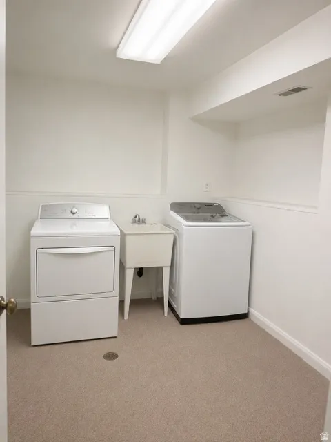 Laundry room featuring neutral carpeting, a utility sink, and overhead fluorescent lighting