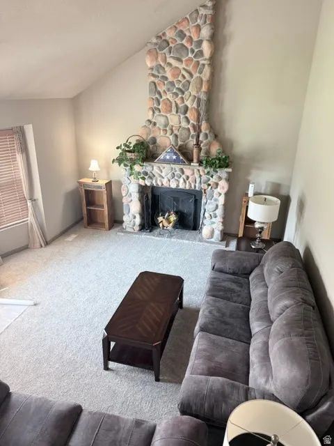 Vaulted ceiling with a full-height stone-clad fireplace featuring a mantel, set on neutral carpeting