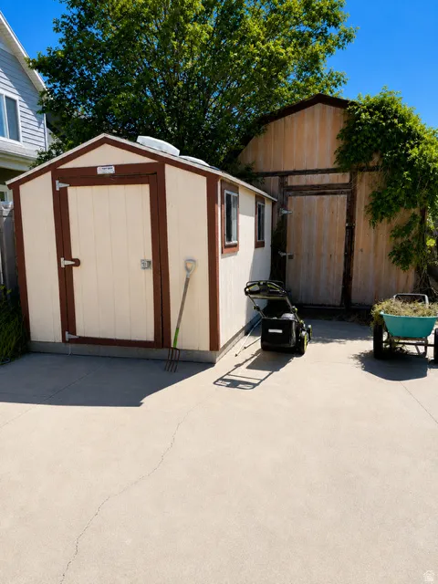 Detached storage shed with double doors and window openings, featuring a light-colored body and dark trim