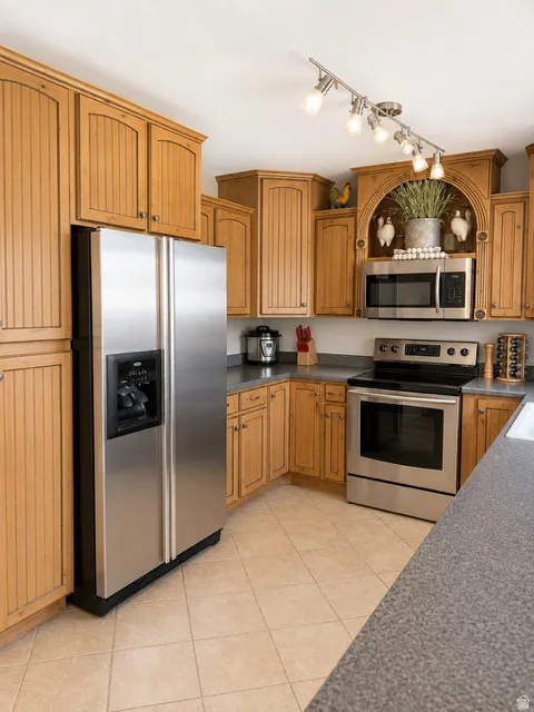 Kitchen featuring light wood cabinetry, stainless steel appliances, speckled gray countertops, and tiled flooring