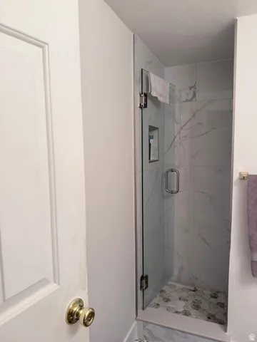 Glass-enclosed shower with a built-in niche, featuring marble-style wall tiles and hexagonal floor tiles